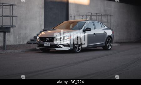 Silberne Limousine auf der Straße im Industrieviertel. Das Viertel von vorne auf den sportlichen Volvo S60, der in einer Stadt in der Nähe einer Betonmauer und eines Notausgangs geparkt ist. Stockfoto