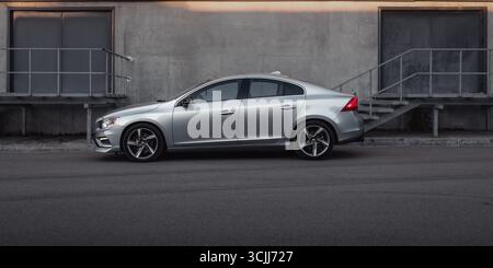Silberne Limousine auf der Straße im Industrieviertel. Seitenprofil des sportlichen Volvo S60, der in einer Stadt in der Nähe einer Betonmauer zwischen zwei Ausgängen geparkt ist. Stockfoto