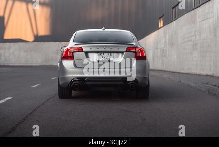 Silberne Limousine auf der Straße im Industrieviertel. Rückansicht des Volvo S60 bei Sonnenuntergang entlang der Lagerwand. Stockfoto