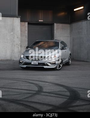 Silberner Volvo S60 in der Nähe der Laderampe (vertikales Bild). Die Vorderansicht der sportlichen Limousine, die neben Betonwänden des Lagerhauses steht. Stockfoto