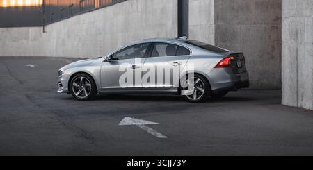 Silberne Limousine auf der Straße im Industrieviertel. Seitenansicht des sportlichen Volvo S60 beim Verlassen eines Lagers bei Sonnenuntergang. Stockfoto