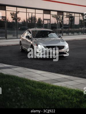 Silver Volvo S60 in einer Straße in der Nähe eines modernen Glasgebäudes. Dreiviertelansicht der schwedischen Sportlimousine, die auf der Außenseite der Straßenkurve geparkt ist. Stockfoto