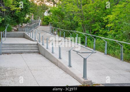 Gehweg mit Geländer und Stufen, die zu einem Gebäude führen. Das Geländer besteht aus Metall und ist an den Stufen befestigt Stockfoto