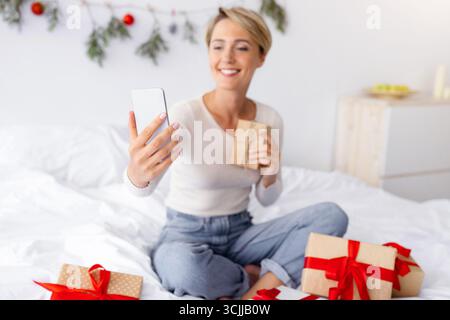 Lady mit Handy macht Videocall auf Weihnachten halten Geschenk Stockfoto
