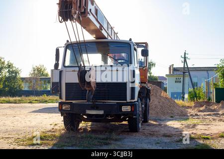 Alter Mobilkran auf einer Baustelle vor dem Hintergrund eines Zauns und eines Sandhaufens am Abend nach der Arbeit. Vorderansicht Stockfoto