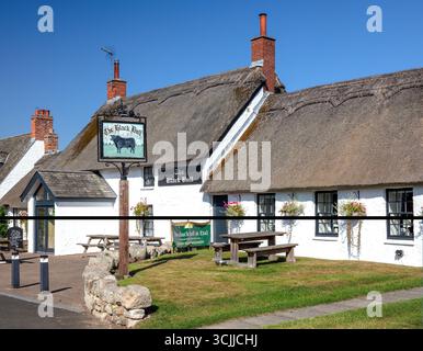 Ein Blick an einem sonnigen Sommertag auf die Hauptstraße des Dorfes Etal in Northumberland bei Berwick, in Richtung des reetgedeckten Pubs The Black Bull Stockfoto