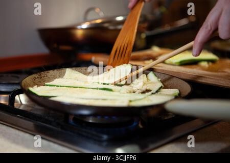 In einer Pfanne gebratene Zucchini-Scheiben werden gerührt und mit einem Holzspachtel gekocht. Hausküche Zubereitung eines vegetarischen Gerichts. Stockfoto