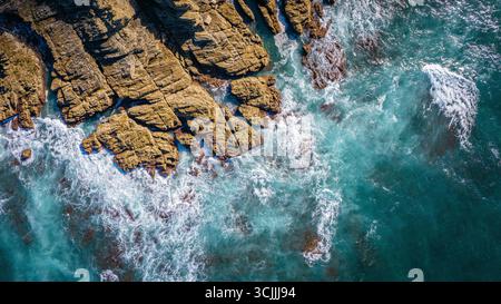Felsen entlang der Küste mit Meereswellen, die von oben zusammenbrechen, zeigen weißen Schaum und türkisfarbenes Wasser, dramatische Meereslandschaft und natürlichen Reisehintergrund Stockfoto