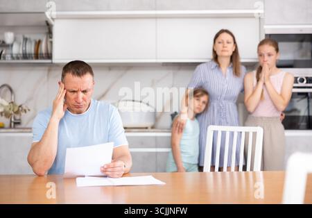 Verärgerter Vater liest sorgfältig Dokumente. Die ganze Familie steht in Angst vor dem Hintergrund Stockfoto