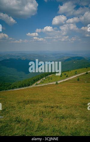 Panoramablick auf die Berge in Griechenland mit sanften grünen Hügeln, offener Wiese und gewundener Straße unter blauem Himmel mit weißen Wolken Stockfoto