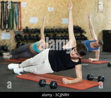 Ein Typ, der beim Gruppentraining im Fitnessstudio die seitliche Plank-Pose hält Stockfoto