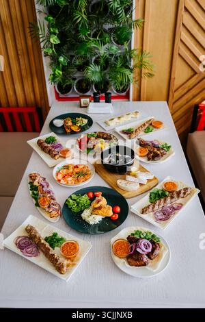 Gegrilltes Fleisch und Gemüse auf Tellern, serviert mit Saucen und frischen Kräutern Stockfoto