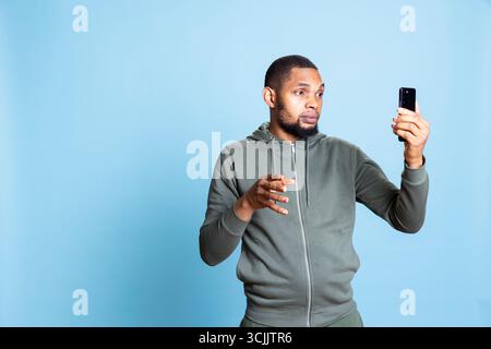 Junge zwanglose, entspannte Person, die mit Freunden im Videonetzwerk diskutiert, mit Freunden vor blauem Hintergrund tratscht, afroamerikanischer Erwachsener positiv und freundlich ist. Stockfoto