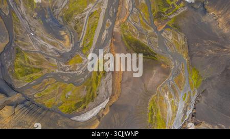 Geflechtenes Gletscherflusssystem in Island von oben gesehen mit gewundenen Wasserkanälen, die durch karges vulkanisches Berggelände führen Stockfoto