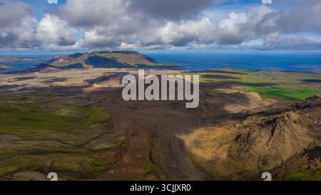Vulkanische Kraterlandschaft in Island mit Bergen, grünen Feldern und dramatischen Wolken über der Küste des Nordatlantischen Ozeans Stockfoto