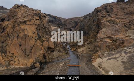 Schmaler Bach schlängelt sich durch hoch aufragende vulkanische Klippen im abgelegenen Hochland Islands mit felsigen Hängen und dramatischen Landschaften Stockfoto