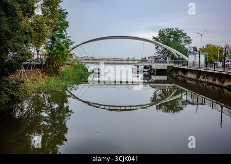 Eine moderne Fußgängerbrücke mit weißem Bogen überspannt einen ruhigen Kanal mit Booten, die an den Ufern in Yalova, Türkei, ankern. Die Reflexion der Brücke ist sichtbar Stockfoto