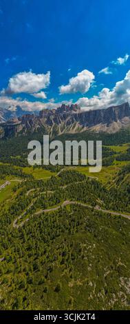Gewundene Straße führt durch die Dolomiten Italien mit üppigen grünen Wiesen, steilen Klippen und dramatischer Berglandschaft unter bewölktem Himmel Stockfoto