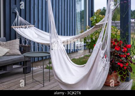 Hängematte in einer ruhigen ländlichen Umgebung, mit weichen Stoffen und bunten Blumen, schaffen einen ruhigen Raum für Entspannung und unbeschwerten Genuss Stockfoto