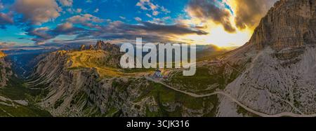 Dolomiten Italien Panoramablick auf den Sonnenuntergang mit den Tre Cime Gipfeln, felsigen Hängen, gewundenen Pfaden und glühendem Himmel, der warmes Licht über die Berge wirft Stockfoto