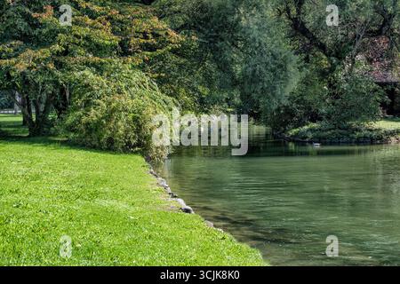 Blick auf den English Park mit einem Fluss, der durch einen grünen Park fließt, an sonnigen Sommertagen. Stockfoto