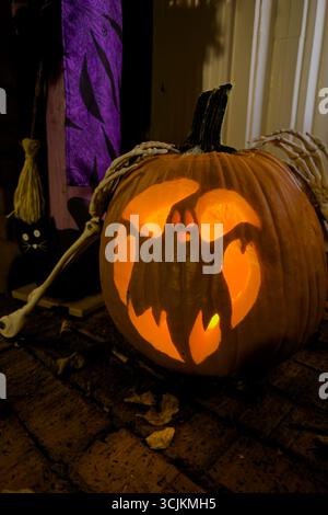 Ein Kürbis, der mit einem Bild eines Geistes geschnitzt ist, leuchtet mit einer orangen Kerze als Teil der Halloween-Dekoration eines Hauses. Stockfoto
