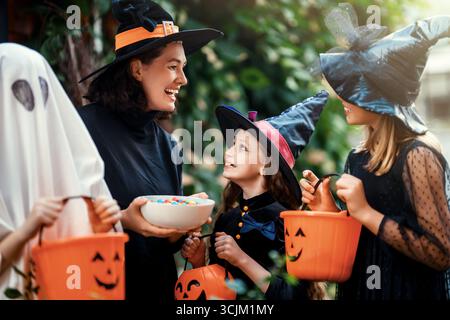 Glückliche Leute feiern Halloween. Erwachsene behandelt Kinder im Freien mit Süßigkeiten. Stockfoto