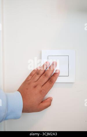 Kinderhand, die einen Lichtschalter an einer weißen Wand drückt Stockfoto