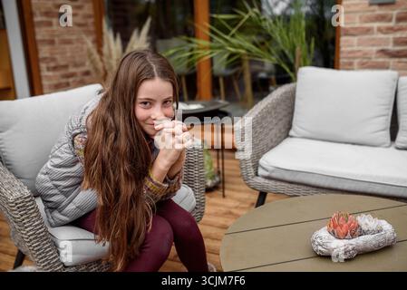 Lächelndes Kind mit langen Haaren, das im Freien Pullover und Weste trägt. Stockfoto