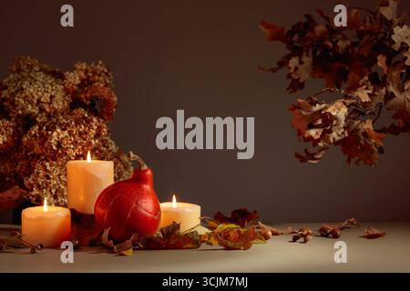 Stillleben mit Kürbis, ausgetrockneten Blättern und brennenden Kerzen. Im Hintergrund getrocknete Hortensienblüten und Eichenzweige. Herbstkonzept. Stockfoto