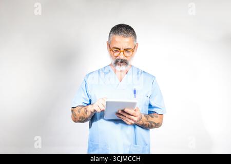 Reifer männlicher Arzt mit blauen Peelings und Brillen, mit digitalem Tablet, die effiziente und moderne Gesundheitsversorgung Stockfoto