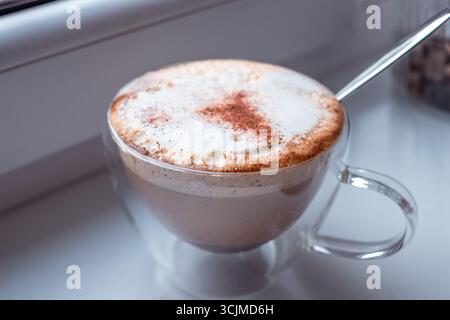 Frischer Cappuccino, serviert in einer transparenten Tasse, mit einer reichhaltigen Schaumschicht und einem Hauch von Zimt, sorgt für ein einladendes und aromatisches Kaffeeerlebnis Stockfoto