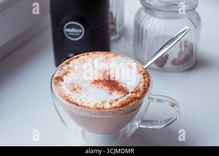 Frischer Cappuccino mit aromatischem Zimt in einer klaren Tasse, der seine schaumige Textur und die cremigen Schichten hervorhebt und ein angenehmes Kaffeeerlebnis für bietet Stockfoto
