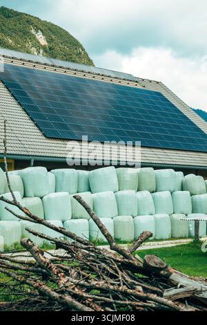 Große grüne Silageballen, die ordentlich entlang eines ländlichen Hofes angeordnet sind, mit Bergen, die hinter den Scheunen aufsteigen. Selektiver Fokus. Stockfoto