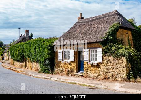 Ein idyllisches, klassisches Strohdach-Cottage mit rustikalem Steinfeld und einer lebhaften blauen Tür befindet sich an einer ruhigen Straße in Abbotsbury, Dorset. Stockfoto