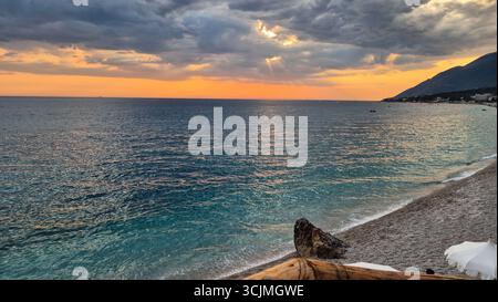 Dramatischer Sonnenuntergang über dem Ionischen Meer vom Strand Dhërmi an einem bewölkten Sommerabend an der albanischen Riviera. Stockfoto