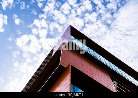 Modernes Bürogebäude mit geometrischer Glasfassade mit offenen Fenstern, starker Symmetrie und reflektierenden Himmelsdetails. Stockfoto