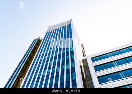 Moderner Hochhaus-Büroturm mit schlanken vertikalen Linien und Glasfassade, die sich vor einem klaren blauen Himmel erhebt. Stockfoto