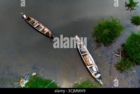 Aus der Vogelperspektive auf zwei verwitterten Kanus, die auf dem ruhigen, dunklen Wasser in der Nähe von grünen Flüssen liegen, Buguma, Rivers State, Nigeria. Stockfoto