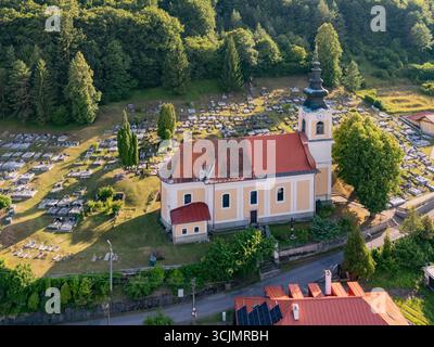 Blick aus der Vogelperspektive auf die Kirche St. Michael Erzengel mit ihrem leuchtend roten Dach und den angrenzenden Friedhof, Vyhne, Region Banská Bystrica, Slowakei. Stockfoto