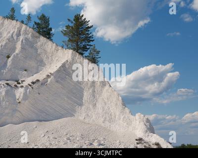 Wunderschöner weißer Berg mit strukturierter Kreideablagerung mit widerstandsfähigen grünen Kiefern vor klarem blauem Himmel und Wolken. Die Natur ist sehr schön Stockfoto