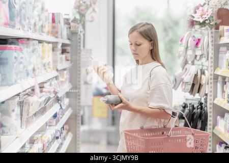 Frau kauft Kosmetik- und Haushaltsartikel ein, während sie die Produktetiketten im Supermarktgang sorgfältig überprüft. Stockfoto