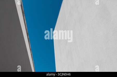 Minimalistische Komposition moderner weißer Wände vor tiefblauem Himmel, die abstrakte geometrische Formen schafft. Die sauberen Oberflächen und scharfen Linien betonen Stockfoto