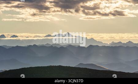 Mehrschichtige Berglandschaft mit goldenen Wolken bei Sonnenuntergang Stockfoto