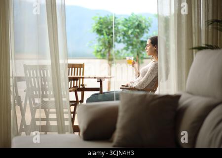 Seitliches Porträt einer Teetrinkenden Frau auf einer Terrasse mit Blick auf zu Hause Stockfoto