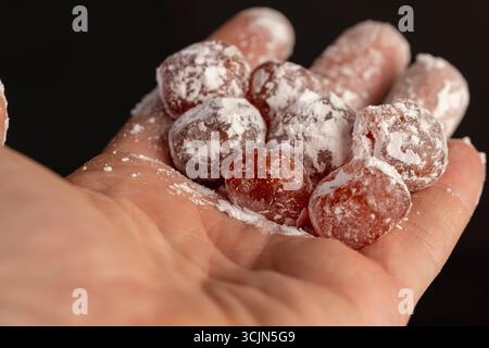 Getrockneter Kumquat und Puderzucker in der Hand, süße getrocknete Orangenkumquatfrüchte in weißem Puderzucker Stockfoto