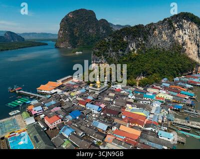 Blick aus der Vogelperspektive auf die pulsierenden Dächer, die sich eng um eine Moschee mit goldener Kuppel gruppieren, eingebettet in die majestätischen Kalksteinklippen in der Bucht von Phang Nga, Ko Panyi, Stockfoto