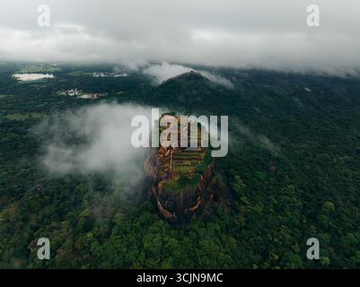 Aus der Vogelperspektive der Felsfestung Sigiriya, die durch ein Meer aus smaragdgrünem Laub unter einer Decke aus ätherischem Nebel durchsticht, Lion Rock, Zentralprovinz, Sri Lanka. Stockfoto