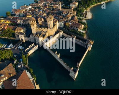 Aus der Vogelperspektive auf die beeindruckenden Steinmauern des Schlosses Scaliger umgeben das türkisfarbene Wasser und bewachen die alte Stadt Sirmione, Verona, Italien. Stockfoto