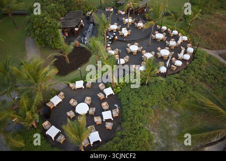 Bambolim, Indien - 16. November 2013: Blick aus der Vogelperspektive auf einen sorgfältig angeordneten Essbereich im Freien, in dem Tische mit weißer Bettwäsche inmitten üppiger Vegetation liegen Stockfoto